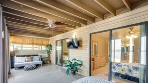 A spacious room with a large bed, a sofa, a TV, and a sliding glass door leading to a bathroom. - Boat Slip & Pool Access at Lake Ozark Condo! (Lake Ozark)