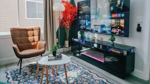 A modern living room with a leather armchair, a round coffee table, a flat-screen TV mounted on the wall, a decorative plant, and a bookshelf.