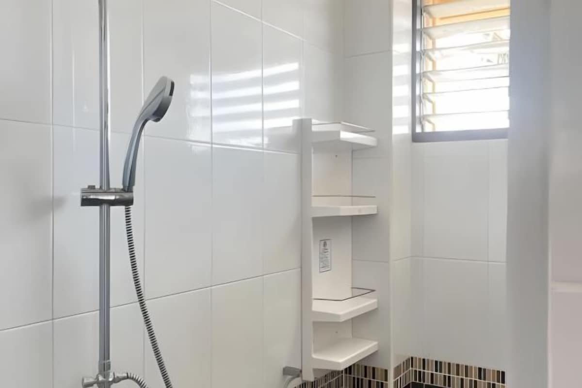 A shower area with a handheld showerhead, a white tiled wall, and a window with blinds.