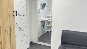 A room with a marble wall, a grey sofa, and a view of a bathroom with a sink and shelves.