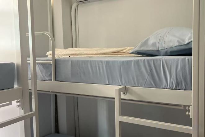 A bunk bed with a mattress and pillow, metal railings, and a small storage compartment.