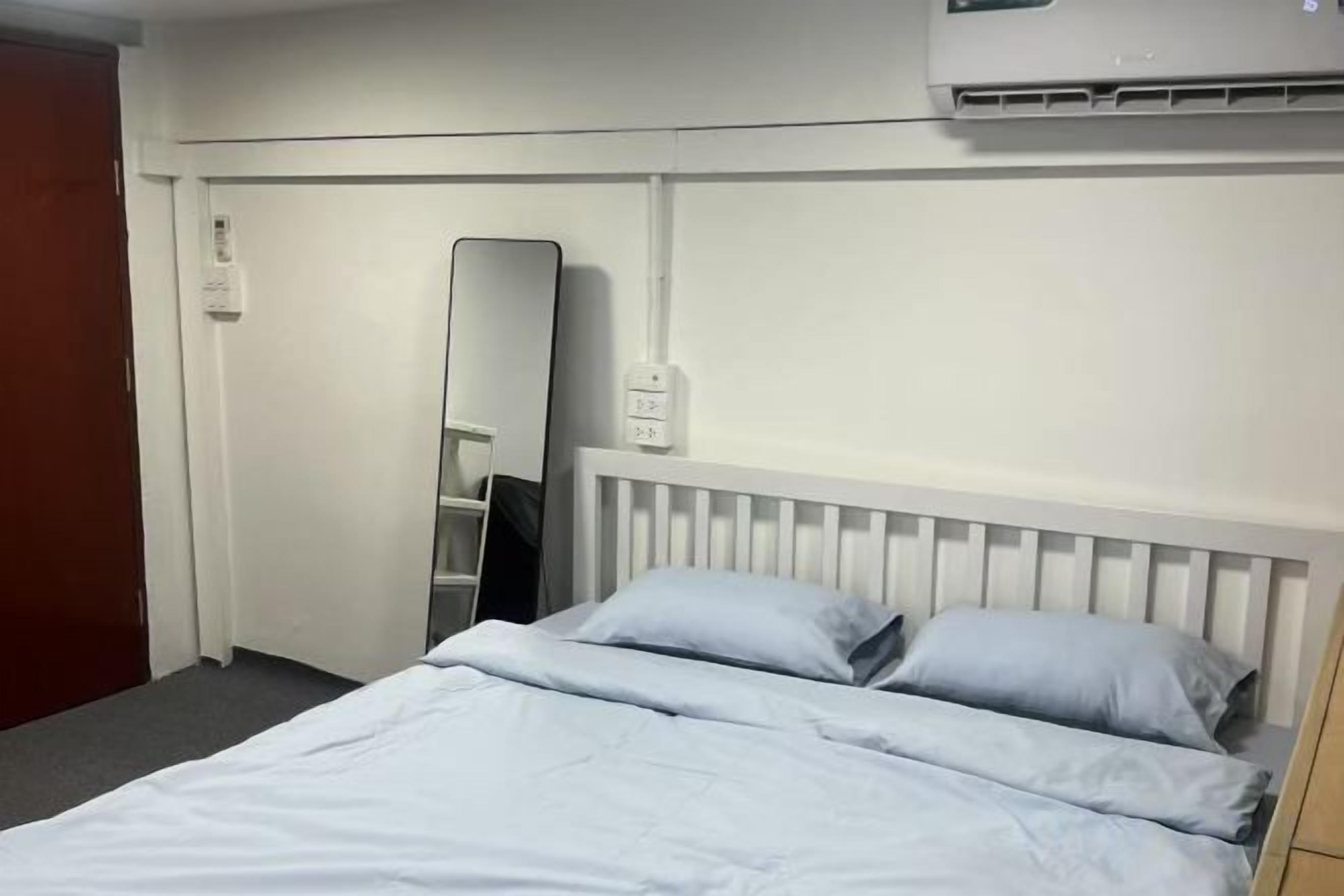 A hotel room with a bed, a mirror, and an air conditioning unit.