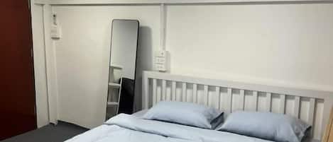 A hotel room with a bed, a mirror, and an air conditioning unit.
