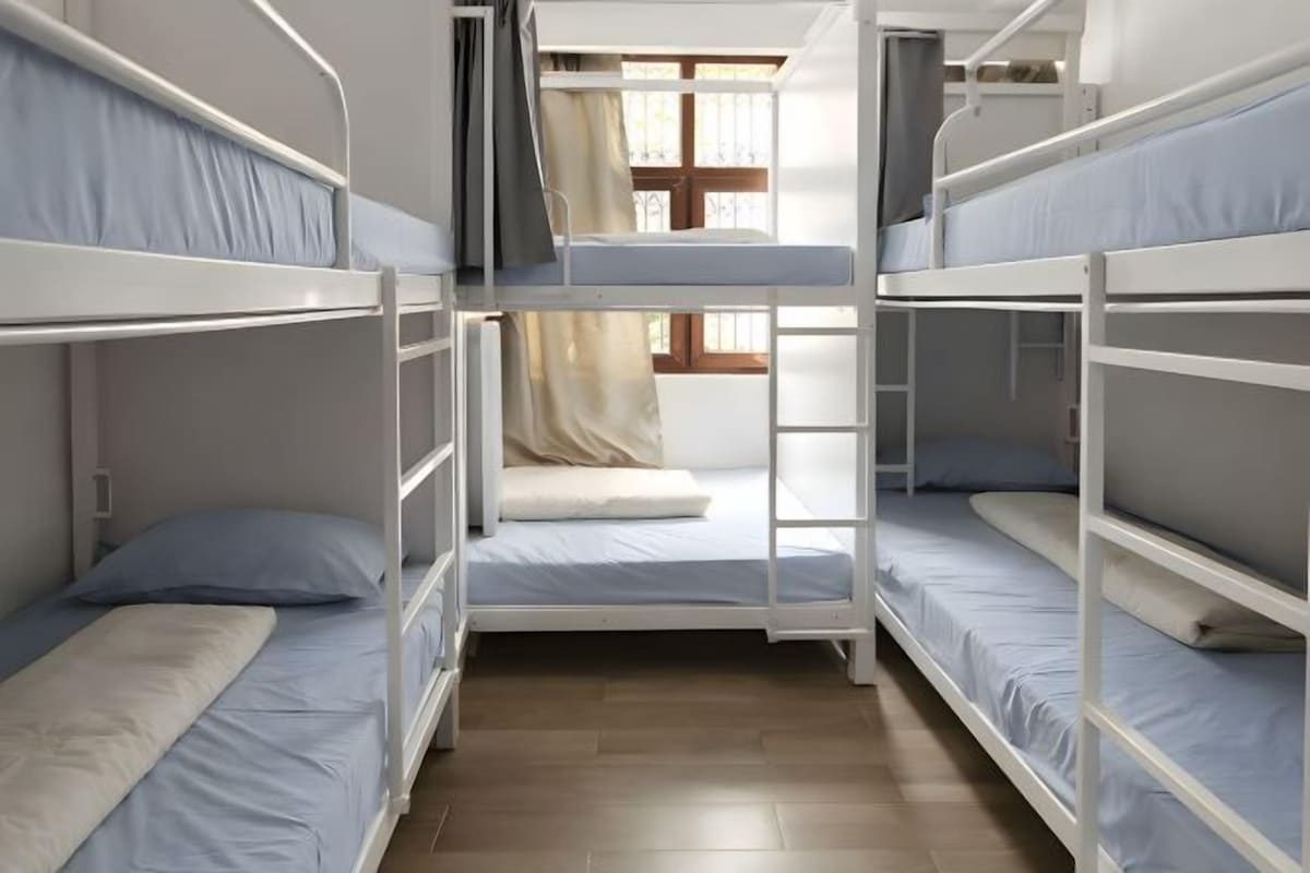A bunk bed room with a television on the upper bunk, a window with curtains, and a wooden floor.