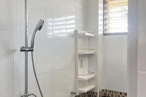 A shower with a handheld showerhead, a wall-mounted shelf, and a window with blinds. - JC Home Stay (Bangkok)