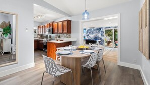 A modern kitchen with wooden cabinets, a central island, and a dining area with a round table and chairs. - MiniGolf/Game Room/Disc Golf/PacMan/Pool Table/Shuffleboard- 9 min to Beach (St. Petersburg)