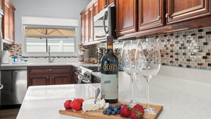 A kitchen with wooden cabinets, a stainless steel refrigerator, a wine bottle, and glasses on a countertop. - MiniGolf/Game Room/Disc Golf/PacMan/Pool Table/Shuffleboard- 9 min to Beach (St. Petersburg)