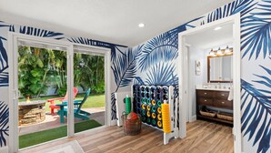 A room with a large sliding glass door leading to a backyard with a fire pit and outdoor furniture. Inside, there is a bathroom with a wooden floor, a mirror, and a sink with a vanity. - MiniGolf/Game Room/Disc Golf/PacMan/Pool Table/Shuffleboard- 9 min to Beach (St. Petersburg)