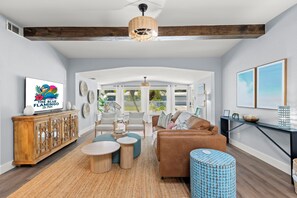 Un salon spacieux avec un plafond haut, des poutres en bois, une grande fenêtre et une vue sur l’extérieur.