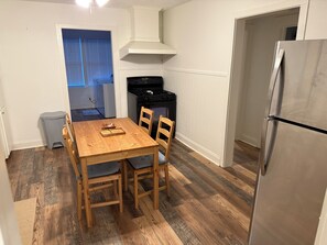 A compact kitchen with a wooden table, chairs, a stove, and a refrigerator.