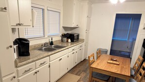 Une cuisine avec des meubles blancs, une machine à café, un évier et une table à manger en bois avec des chaises.