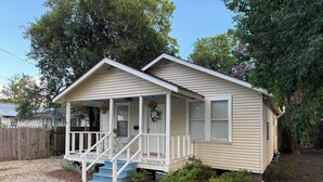 Une maison de plain-pied avec un porche à l’avant, un petit jardin devant et une clôture en bois.