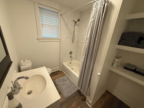 A bathroom with a sink, toilet, shower, and a window.