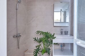 Un baño con ducha, lavabo, espejo y una planta en maceta.