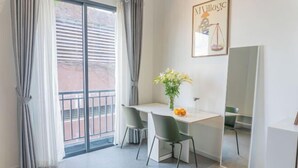 Une chambre moderne équipée d’un bureau, de deux chaises, d’un vase avec des fleurs, d’un grand miroir et d’une fenêtre avec des rideaux.