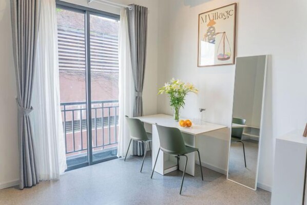 A modern room with a desk, two chairs, a vase with flowers, a large mirror, and a window with curtains. - Express by M Village Le Van Sy, a brand of Modern Village Lifestyle (Ho Chi Minh City)