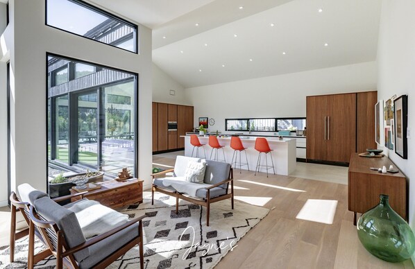 A modern kitchen with a central island, wooden cabinets, and a large window overlooking a garden. - Luxurious new 4 bed 5 bath home (The Blue Mountains)