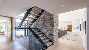A modern interior with a spiral staircase against a stone wall, a living area with a sofa, and a view through a glass door. - Luxurious new 4 bed 5 bath home (The Blue Mountains)
