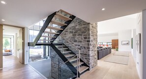 A modern interior with a spiral staircase against a stone wall, a living area with a sofa, and a view through a glass door. - Luxurious new 4 bed 5 bath home (The Blue Mountains)