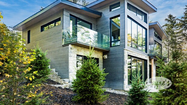 A modern two-story house with a stone foundation, large windows, and a balcony.