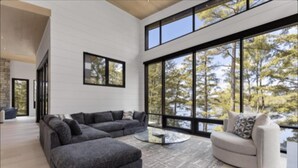 A modern living room with a sectional sofa, a round coffee table, and a view of trees through large windows.