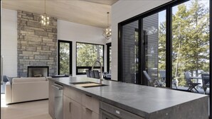 A modern kitchen with a stone fireplace, large windows, and a dining area with outdoor seating.