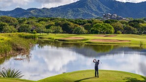 Un campo de golf con un estanque, árboles y una montaña al fondo.