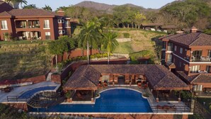 Un resort con una amplia piscina, varias edificaciones y un paisaje montañoso al fondo.
