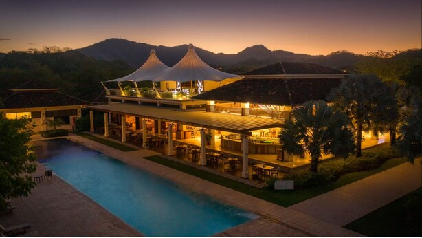 Un resort con piscina, zona de comedor al aire libre y una amplia estructura cubierta.
