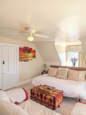 A bedroom with a bed, a ceiling fan, a wall-mounted painting, a window with curtains, and a wooden chest. - Charming Apt Walkable to Shop, Eat & NYC Transport (Montclair)