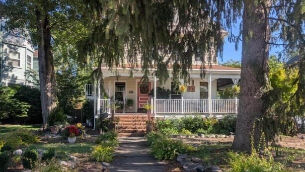 A two-story house with a front porch, a pathway leading to the entrance, and a garden with various plants and flowers. - Sunny & Comfortable: Walk To Shop, Eat & NYC Train (Montclair)