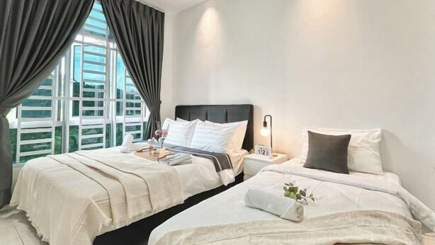 Et hotelværelse med to senge, et stort vindue med gardiner, et sengebord med lampe, og udsigt til grønne områder.