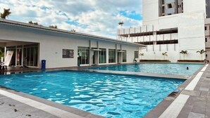 En swimmingpool ved siden af en bygning med moderne design, store vinduer og et overdækket område med siddepladser.