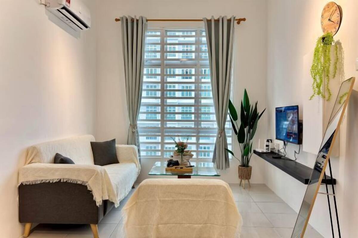 Un salon moderne avec un canapé, une table basse, un téléviseur et une grande fenêtre agrémentée de rideaux.