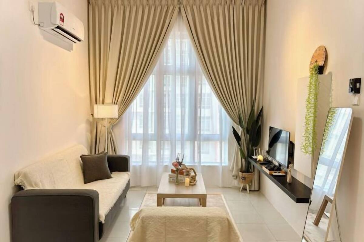 Un salon moderne avec un canapé, une table basse, un téléviseur et une grande fenêtre avec des rideaux.