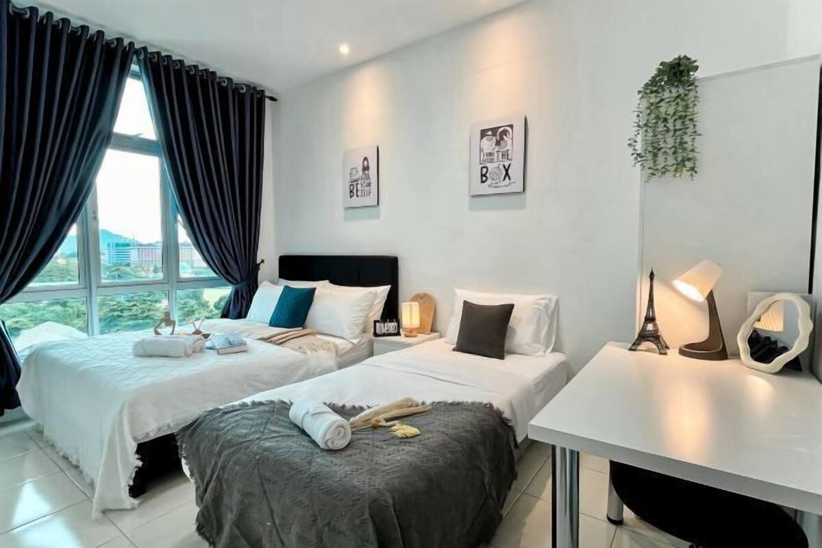 Une chambre d’hôtel avec deux lits, un bureau et une grande fenêtre avec des rideaux.