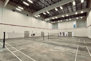 Un court de tennis intérieur spacieux, doté d’un plafond haut et de nombreux luminaires.