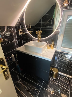 A bathroom with a white sink, black marble tiles, gold fixtures, and a round mirror. - House with a heated pool and spa, 1 hour from Paris and 10 minutes from downtown (Saran)
