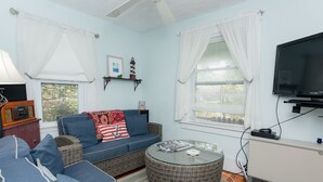 Ein Wohnzimmer mit einem blauen Sofa, einem Korbtisch und einem an der Wand befestigten Fernseher.