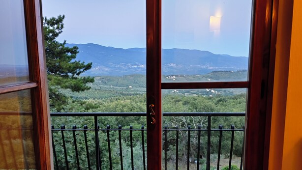 Une porte en bois donne sur un balcon agrémenté d’une rambarde en métal, d’où l’on peut admirer un paysage montagneux et une végétation luxuriante.