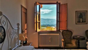 Une chambre avec une grande fenêtre, un radiateur, un lit et deux chaises.