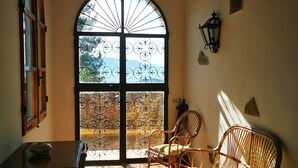 Une pièce dotée d’une grande fenêtre en arc de cercle, d’une table en bois, de deux chaises en osier et d’une lanterne fixée au mur.