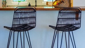 A kitchen with two black wireframe bar stools, a wooden countertop, and two yellow pendant lights. - Tropical Oasis w/ Cenote & Pool – Walk to Beach (Playa del Carmen)