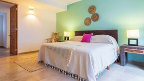 A bedroom with a bed, two bedside tables, a nightstand, a wall-mounted lamp, and a door. - Tropical Oasis w/ Cenote & Pool – Walk to Beach (Playa del Carmen)