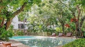 A pool area with lounge chairs, a wooden deck, and lush greenery. - Tropical Oasis w/ Cenote & Pool – Walk to Beach (Playa del Carmen)