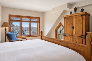 A bedroom with a large bed, a wooden wardrobe, a chair, and a window with a view of snow-covered trees. - Tremblant Prestige - Altitude 172-11 (Mont-Tremblant)
