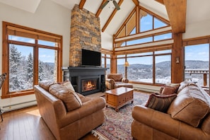 A spacious living room with a stone fireplace, leather sofas, and large windows offering a view of a snowy landscape. - Tremblant Prestige - Altitude 172-11 (Mont-Tremblant)
