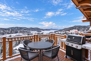 A deck with a table and chairs, a barbecue grill, and a snowy landscape view.