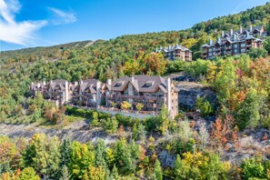Ein mehrstöckiges Jagdhaus mit Steinaußenwand, umgeben von Herbstlaub vor einer hügeligen Landschaft.