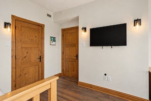 A hallway with wooden doors, a mounted flat-screen TV, and wall-mounted light fixtures. - Tremblant Prestige - Altitude 172-11 (Mont-Tremblant)